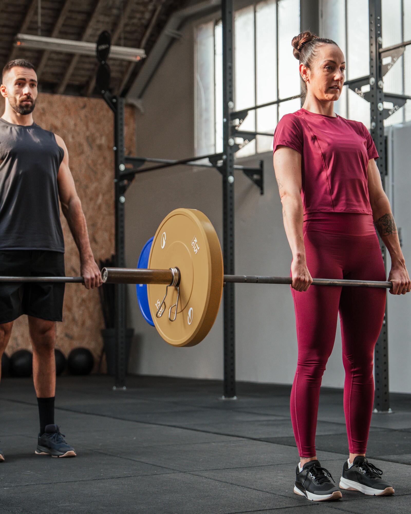 Mann und Frau führen synchron Kreuzheben mit Langhanteln in einem Fitnessstudio aus.