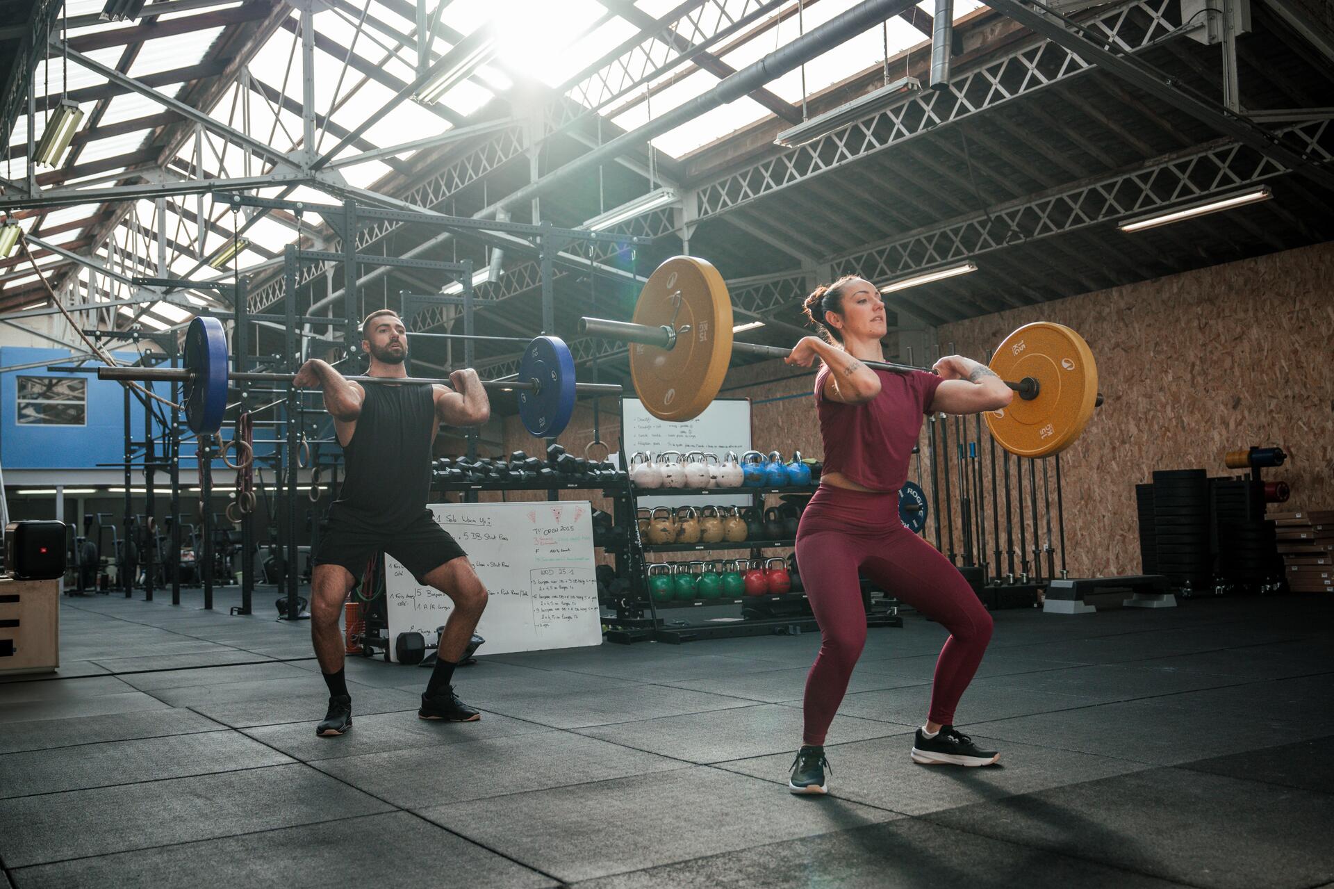 Kobieta i mężczyzna w odzieży fitness ćwiczący ze sztangami w sali treningowej