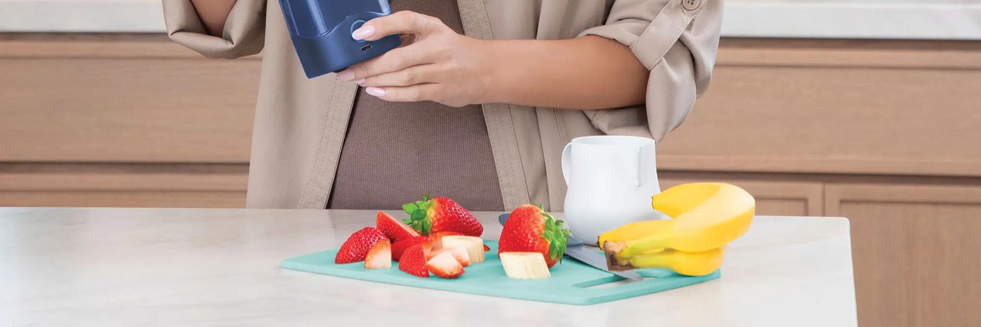 Kobieta przygotowująca shakea z owoców w shakerze na stole pokrojone truskawki banan
