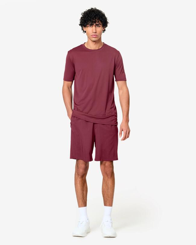 Junger Mann in weinrotem T-Shirt und passenden Shorts, weiße Socken und Schuhe.