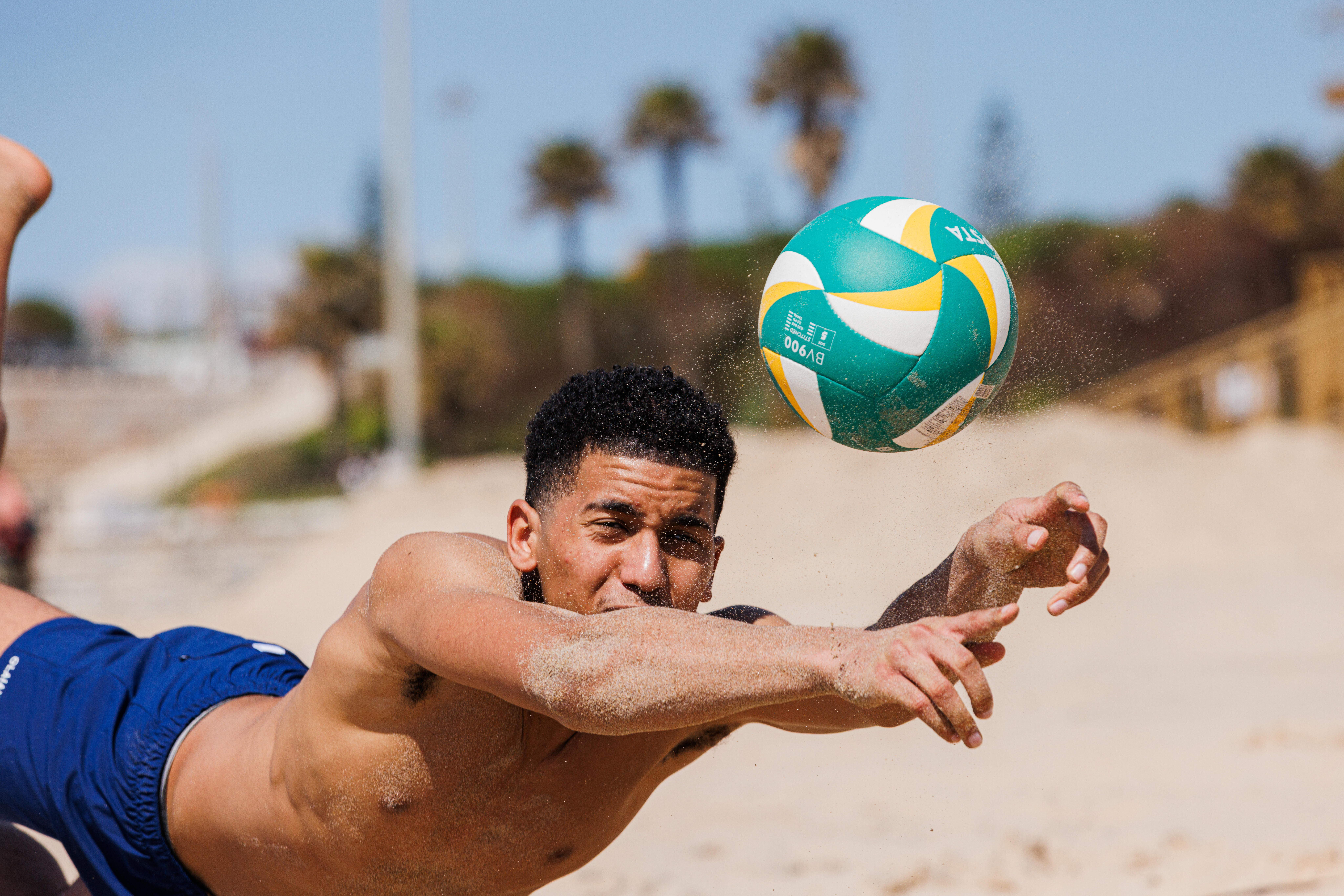 Player diving across the sand to return a beach volleyball.