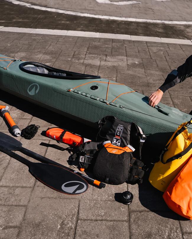 Grünes Kajak, orange Paddel und Zubehör auf grauem Pflastersteinboden, gelber und orangefarbener Packsack.