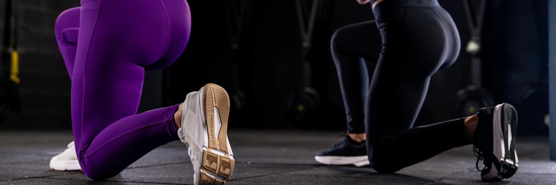 Sportlerinnen führen eine tiefe Kniebeuge im dunklen Fitnessstudio aus