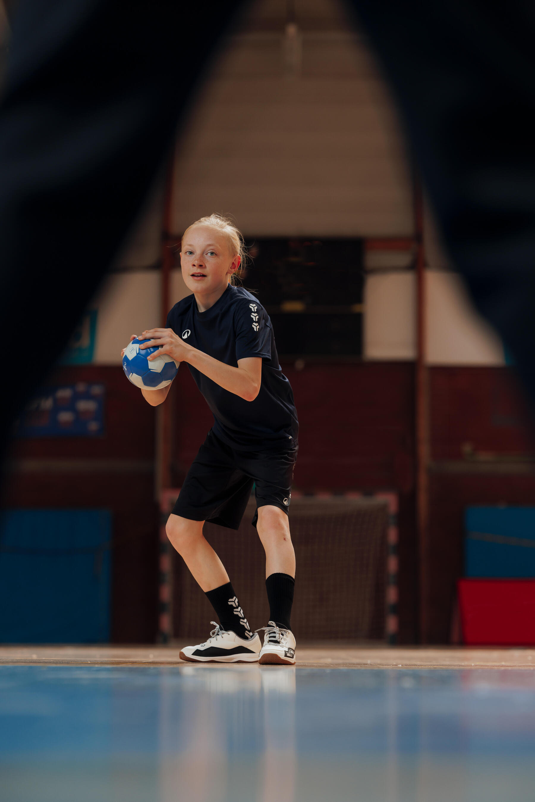 Kind steht mit einem Hanball in einer Sporthalle