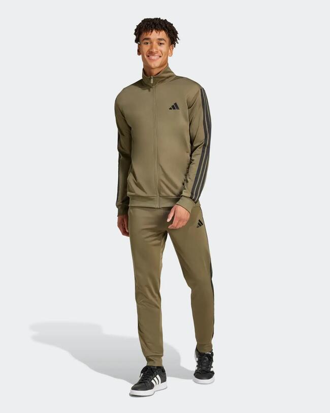 Lächelnder Mann in grünem Adidas-Trainingsanzug mit dunklen Streifen, steht frontal zur Kamera.