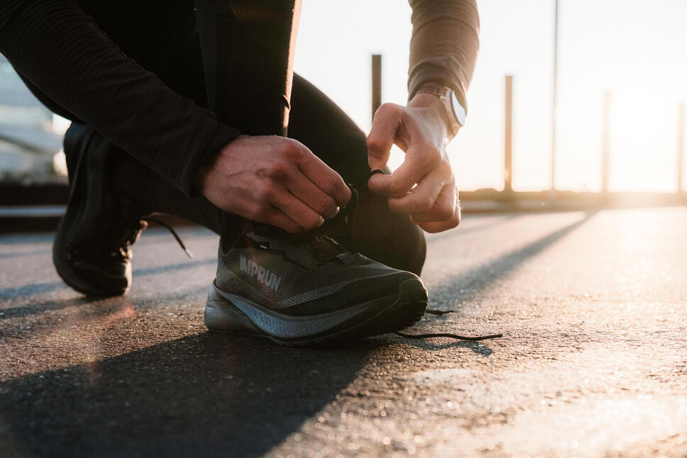 Trkač koji vezuje pertle na crnim Kiprun patikama na asfaltu tokom izlaska sunca