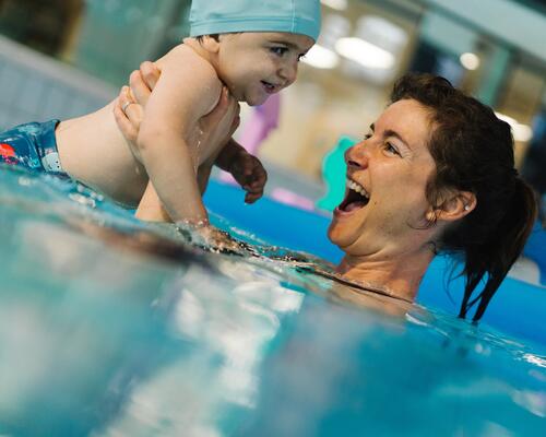 Mama trzymająca niemowlę pod paszkami w czepku w basenie