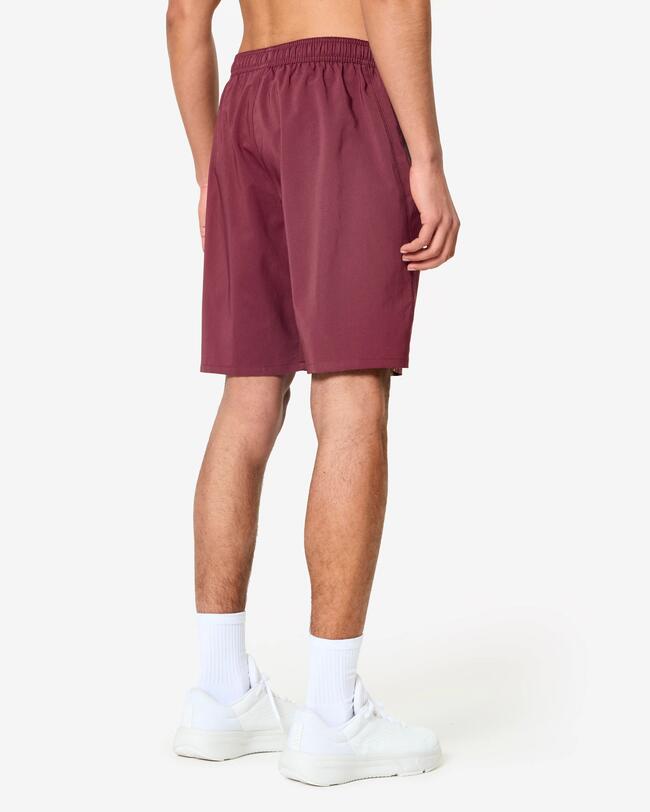 Rückenansicht eines Mannes in weinroten Sportshorts, weißen Socken und weißen Schuhen.