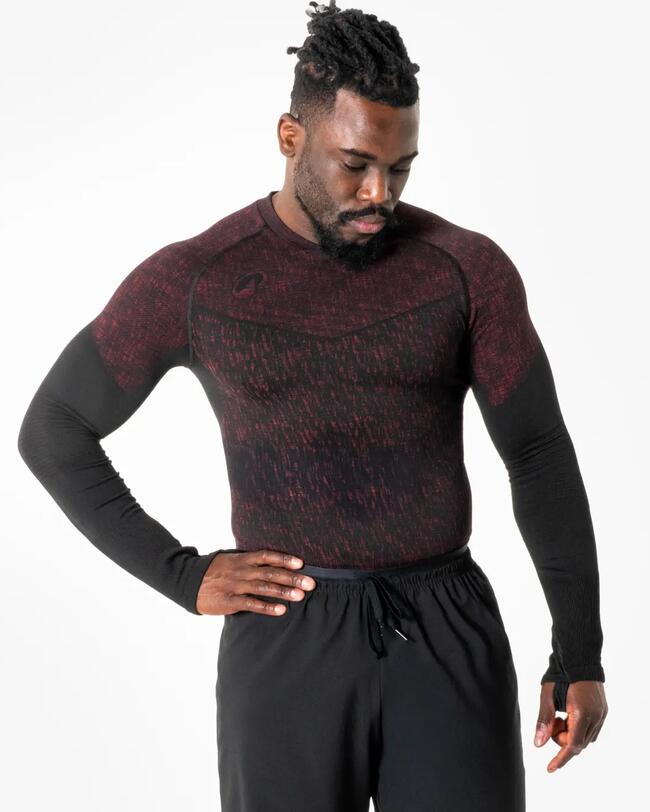 Mann mit bordeaux-schwarzem Keepdry-Langarmshirt vor weißem Hintergrund. Er hält einen Arm an der Hüfte und schaut nach unten.