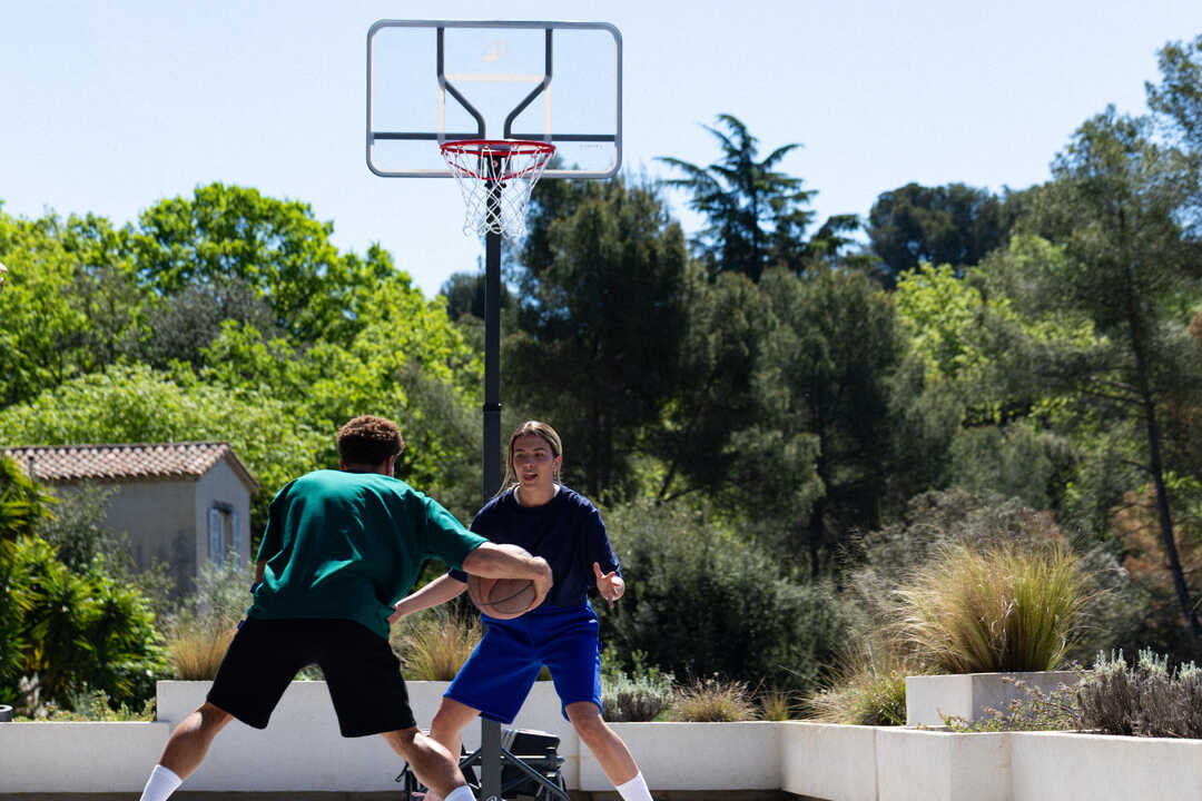 Dečak i devojka igraju košarku na otvorenom terenu ispred Tarmak B500 Easy Box koša.