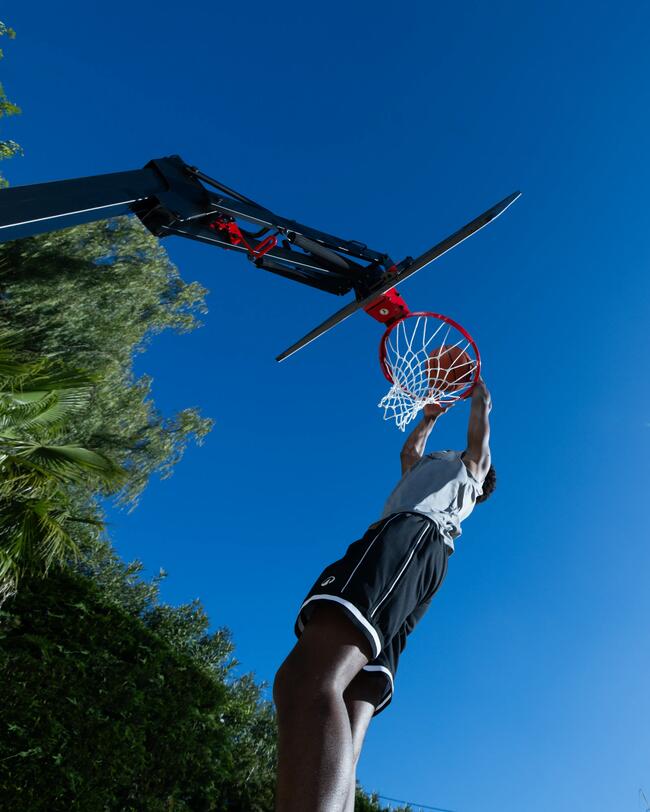 Klappbarer, mobiler Basketballkorb mit Ständer vor blauem Himmel; rote, weiße und schwarze Details.