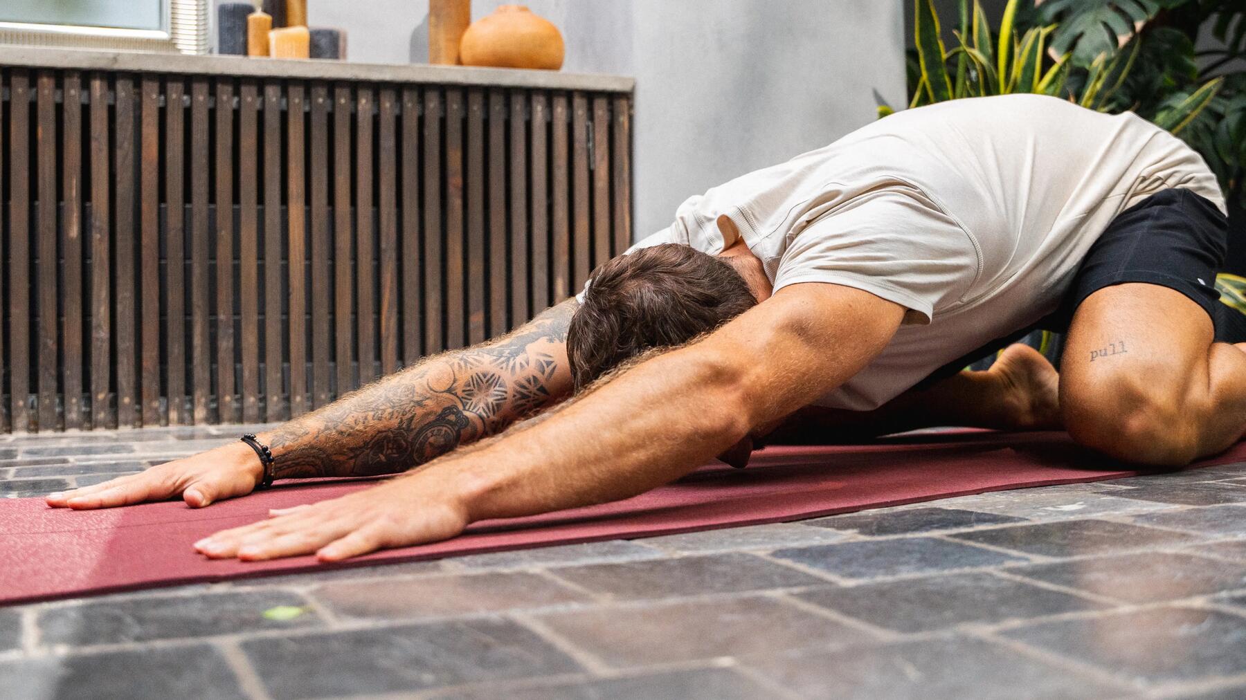 Mann praktiziert Asana auf dem Boden auf einer roten Yogamatte