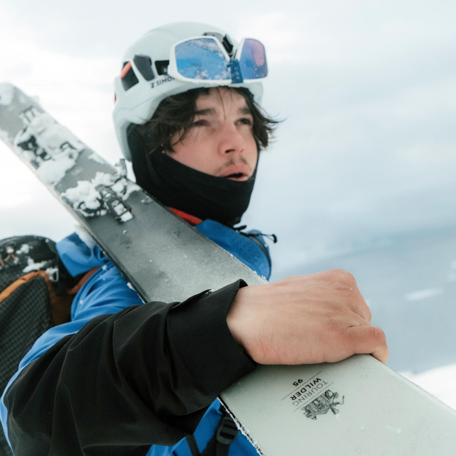 Ein Mann trägt seine Skier und trägt Skibekleidung