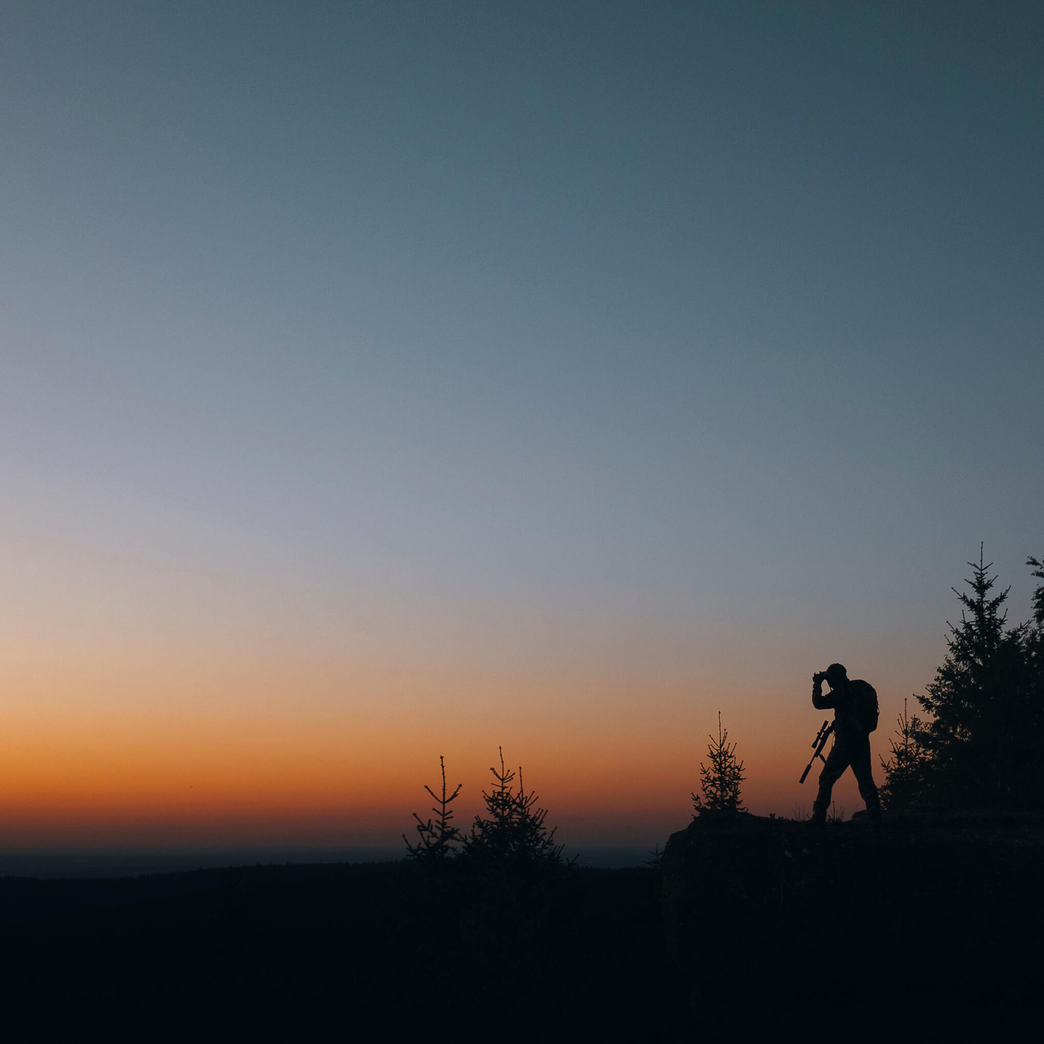 un chasseur à l'approche qui observe aux jumelles alors que le crépuscule est tombé