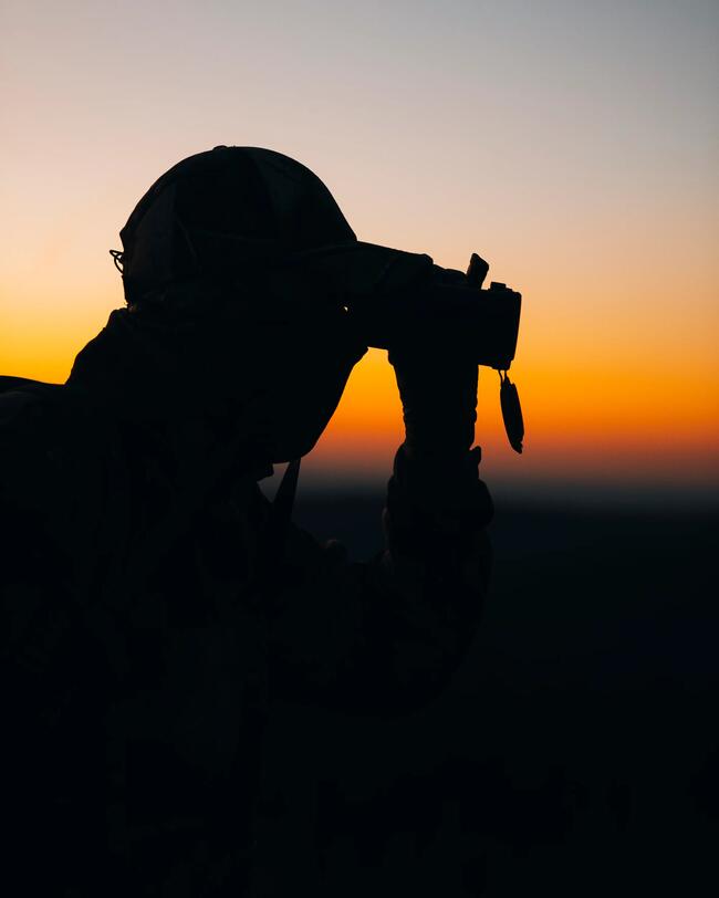 A hunter with HTR binoculars in their hands observes as the sun sets