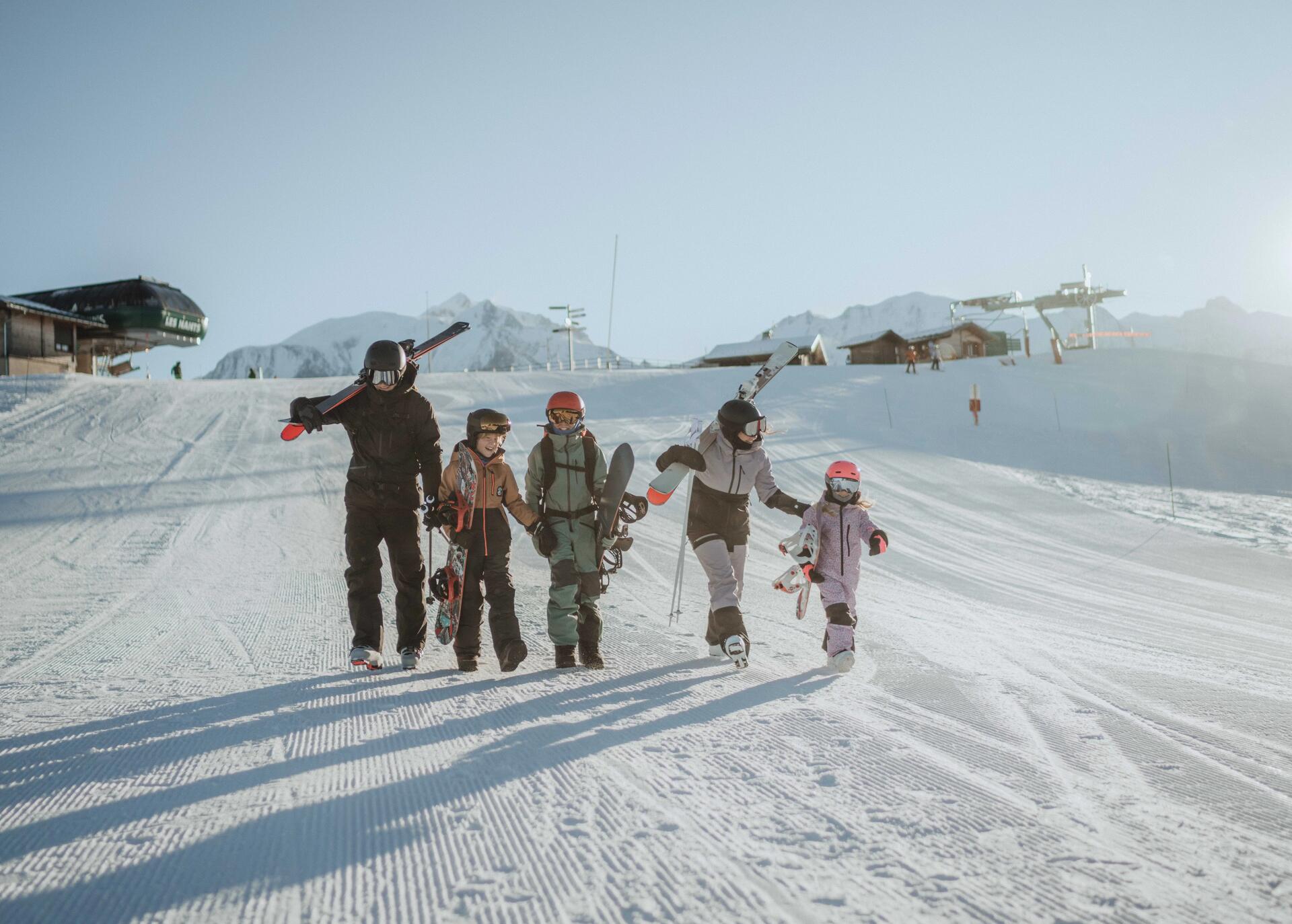Rodzina ze sprzętem narciarskim i snowboardowym idąca po stoku narciarskim we Włoszech