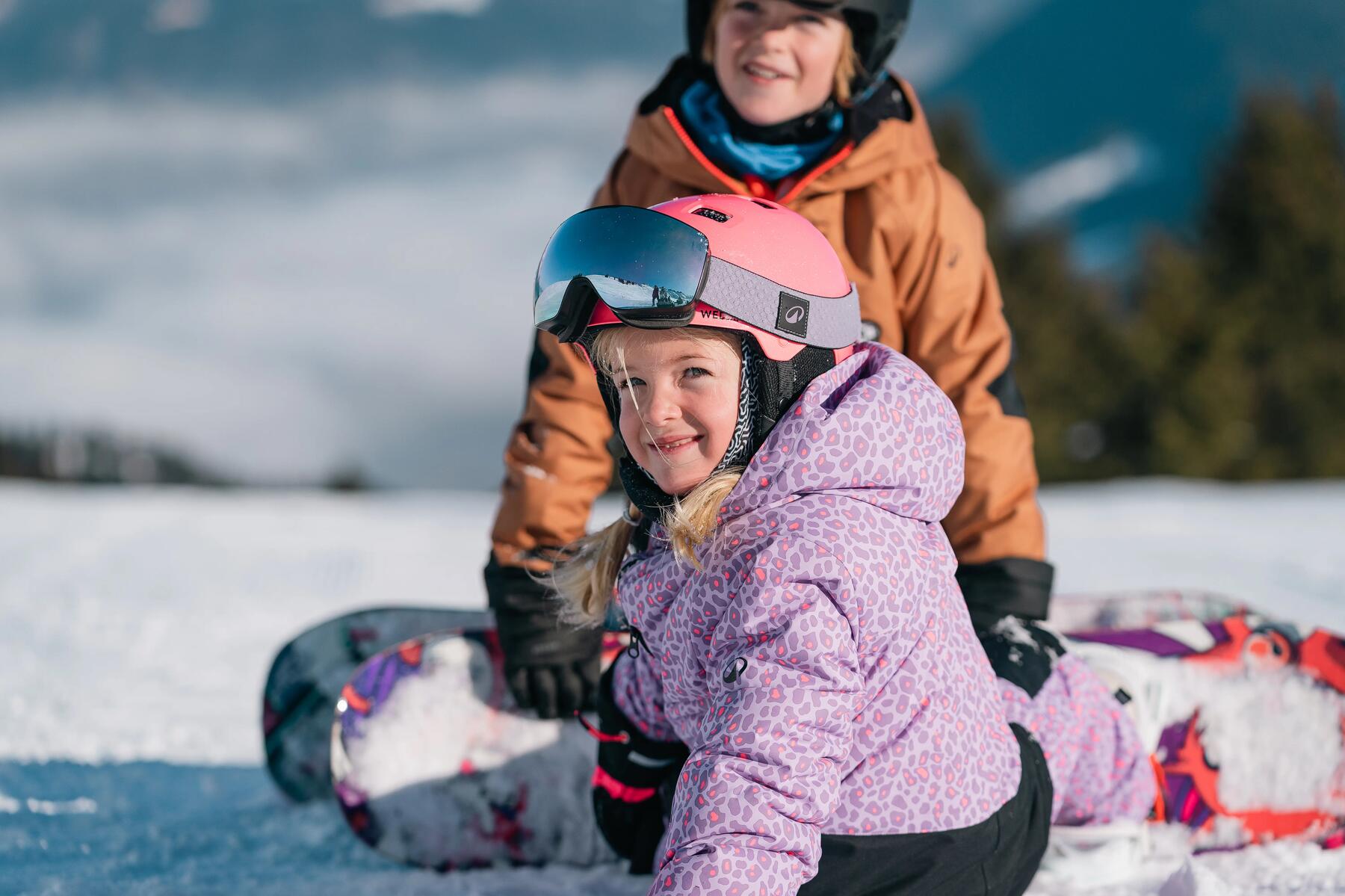 Dzieci siedzące na śniegu z przypiętymi deskami snowboardowymi