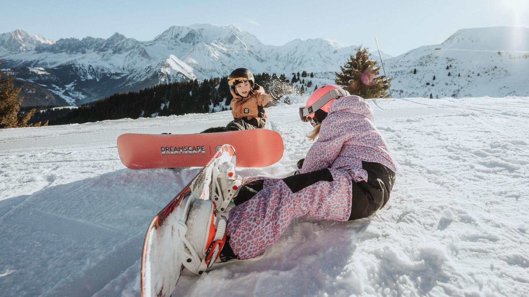 Dzieci w kaskach i odzieży snowboardowej odpoczywające na stoku z przypiętymi deskami snowboardowymi