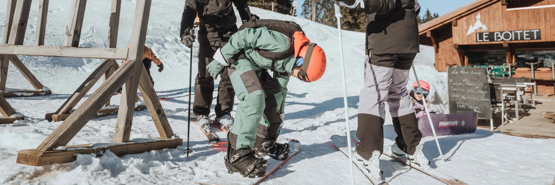 Rodzina w odzieży do sportów zimowych zastanawiająca się co jest łatwiejsze narty czy snowboard stojąc przed barem na stoku