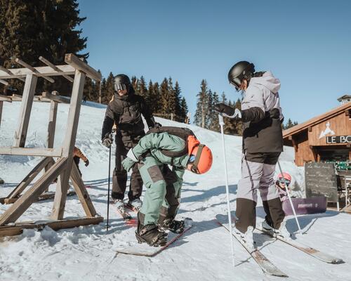 Rodzina w odzieży do sportów zimowych zastanawiająca się co jest łatwiejsze narty czy snowboard stojąc przed barem na stoku
