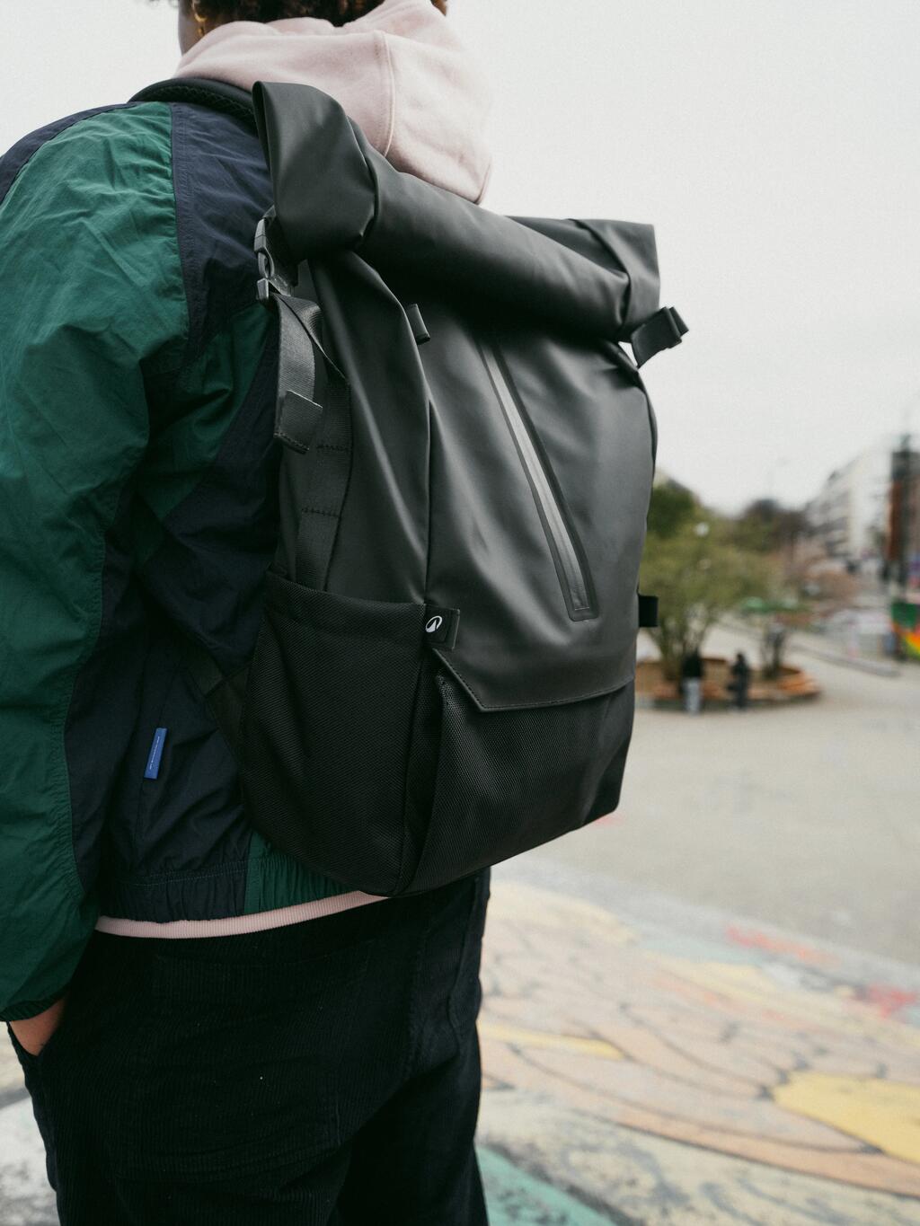 Ein Mann am Gehsteig stehend. Man sieht ihn nur von hinten und der schwarze Rucksack steht im Mittelpunkt