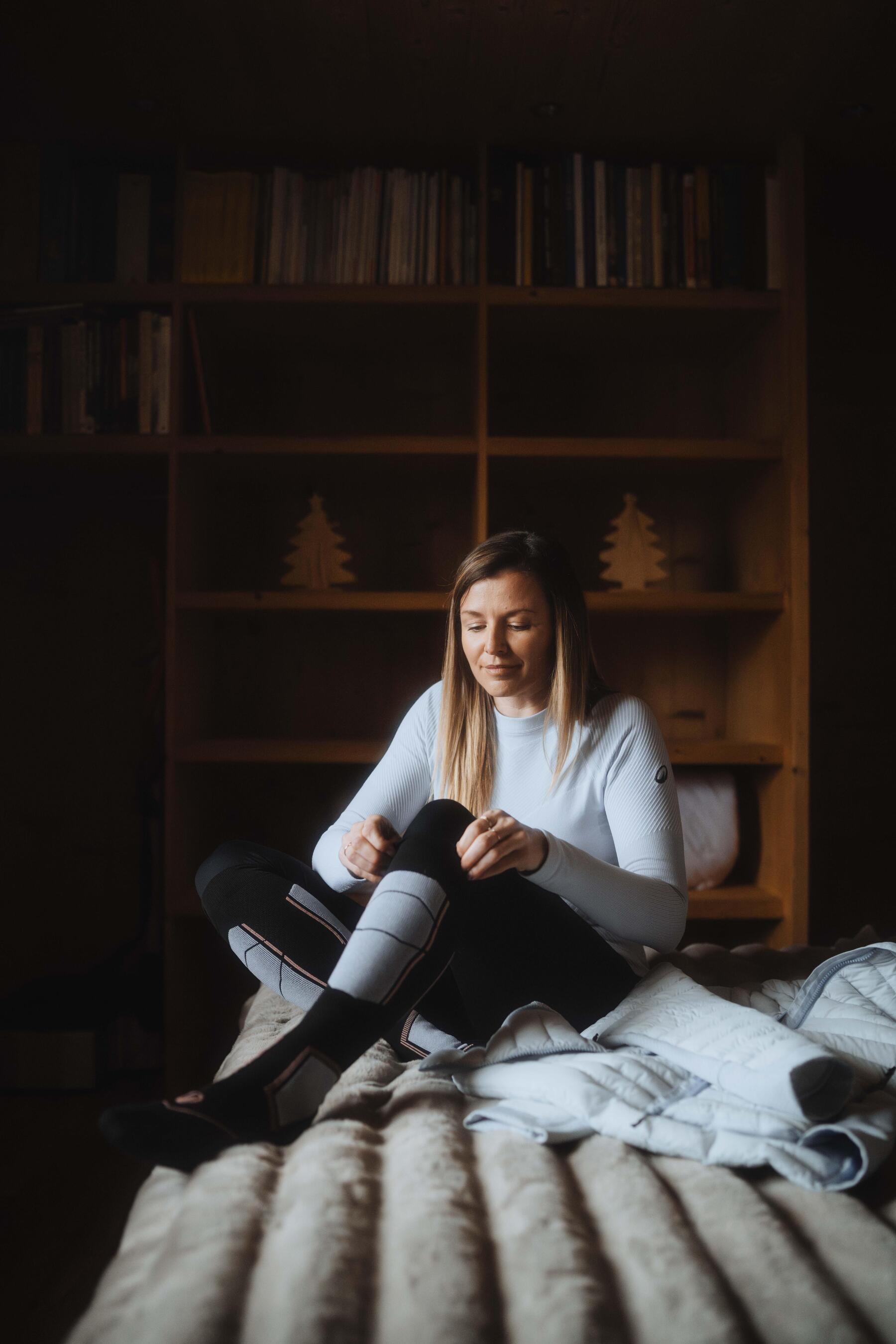 une femme assise sur un lit enfile des chaussettes de ski decathlon