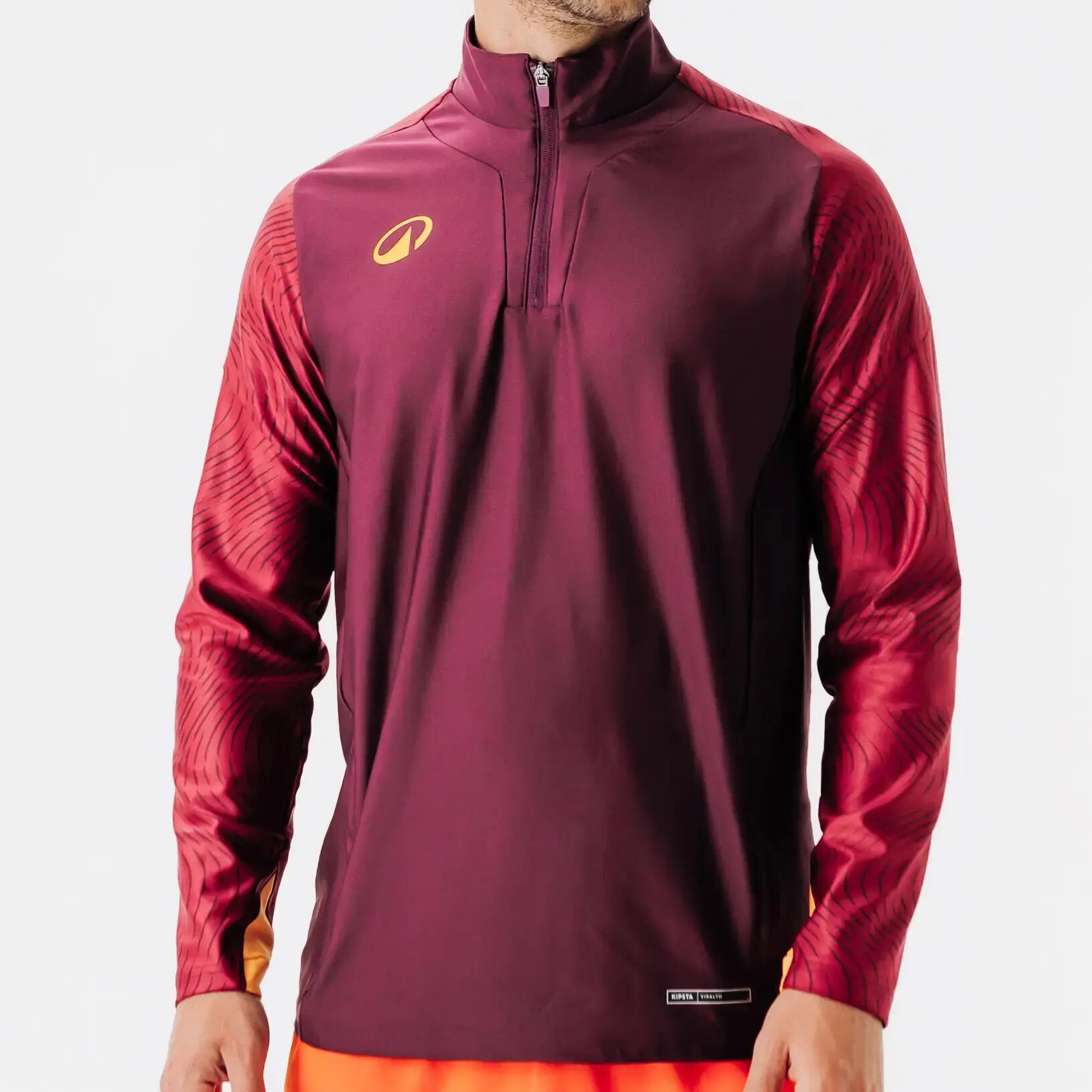 Mann in bordeaux rotem Half-Zip-Sweatshirt vor weißer Wand.