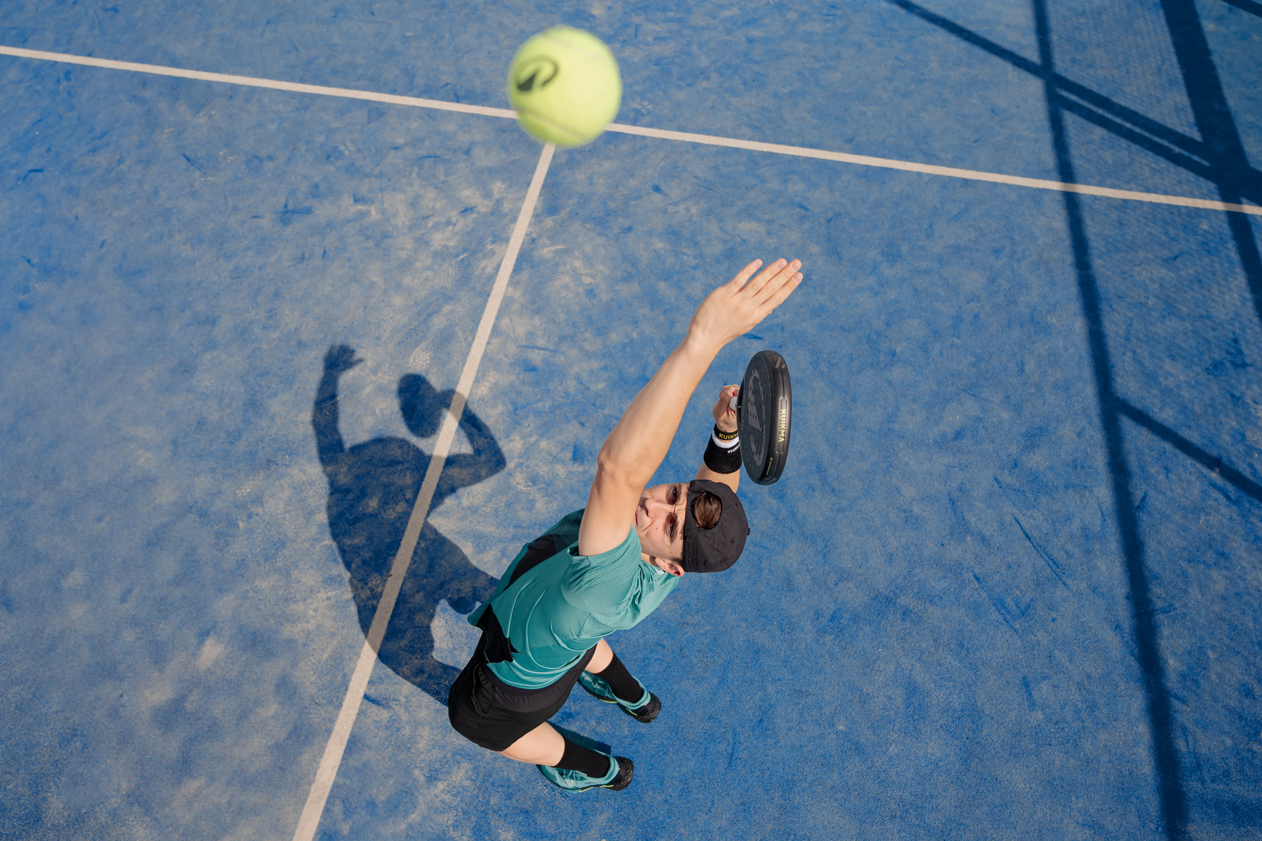 Ein männlicher Padelschläger schlägt den Ball auf dem Platz mit einer Bewegung von unten nach oben.
