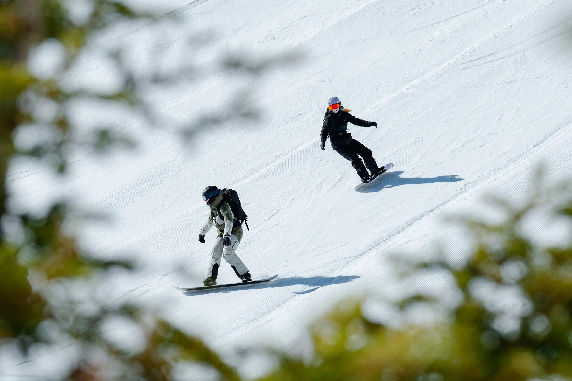 Dwie osoby w kaskach i w goglach jeżdżące na snowboardzie