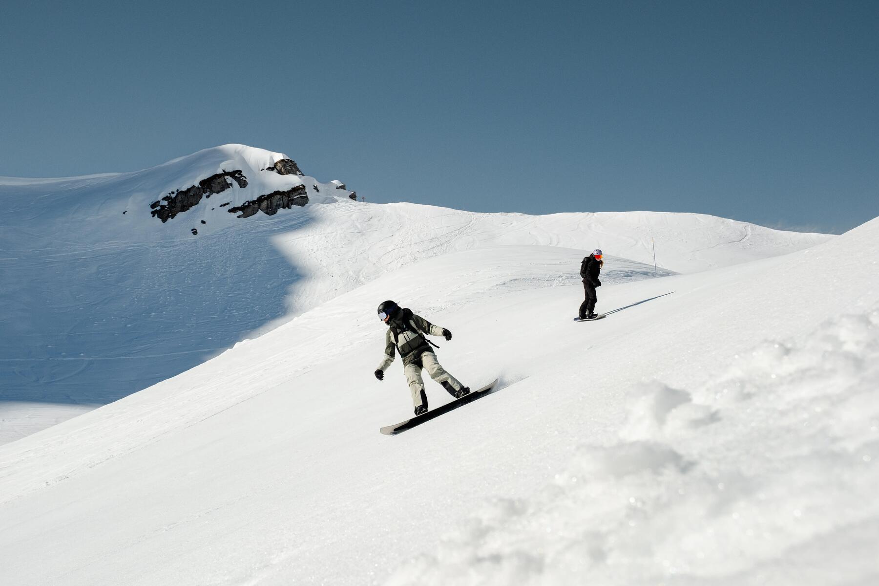 Dwie osoby w kasku i w goglach jeżdżące na snowboardzie