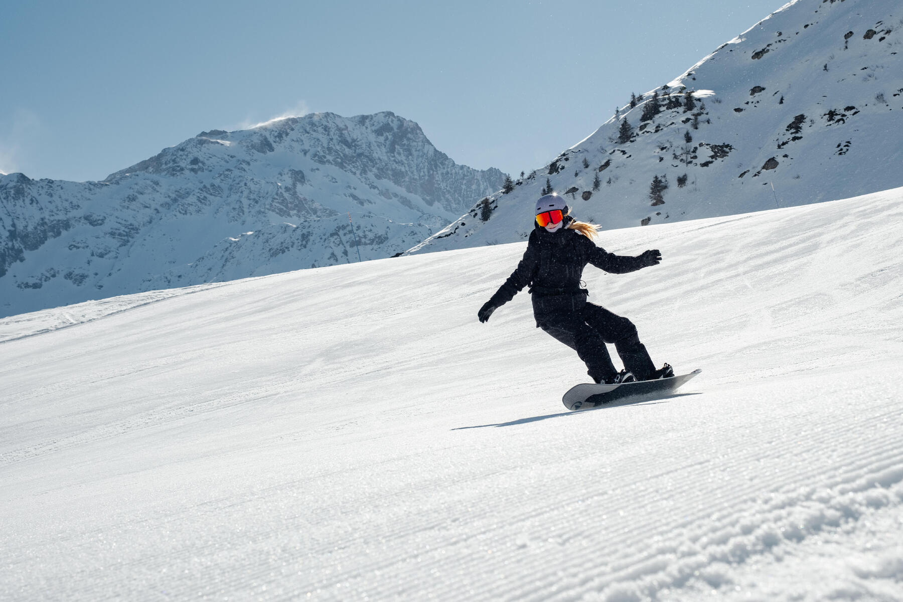 Kobieta w odzieży zimowej w kasku jeżdżąca na desce snowboardowej