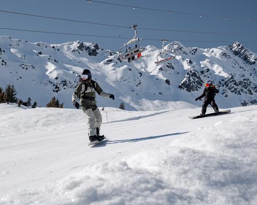 Kobieta z instruktorem narciarstwa w kaskach i w goglach jeżdżący na snowboardzie na stoku