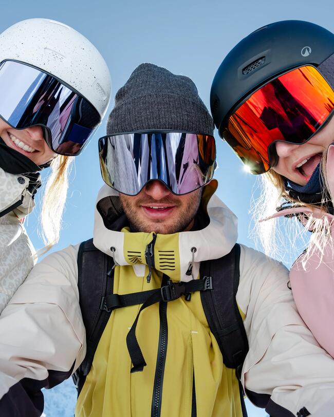 Zwei Frauen und ein Mann in Skimontur inklusive Skihelmen und Skibrillen stehen nebeneinander und schauen in die Kamera.