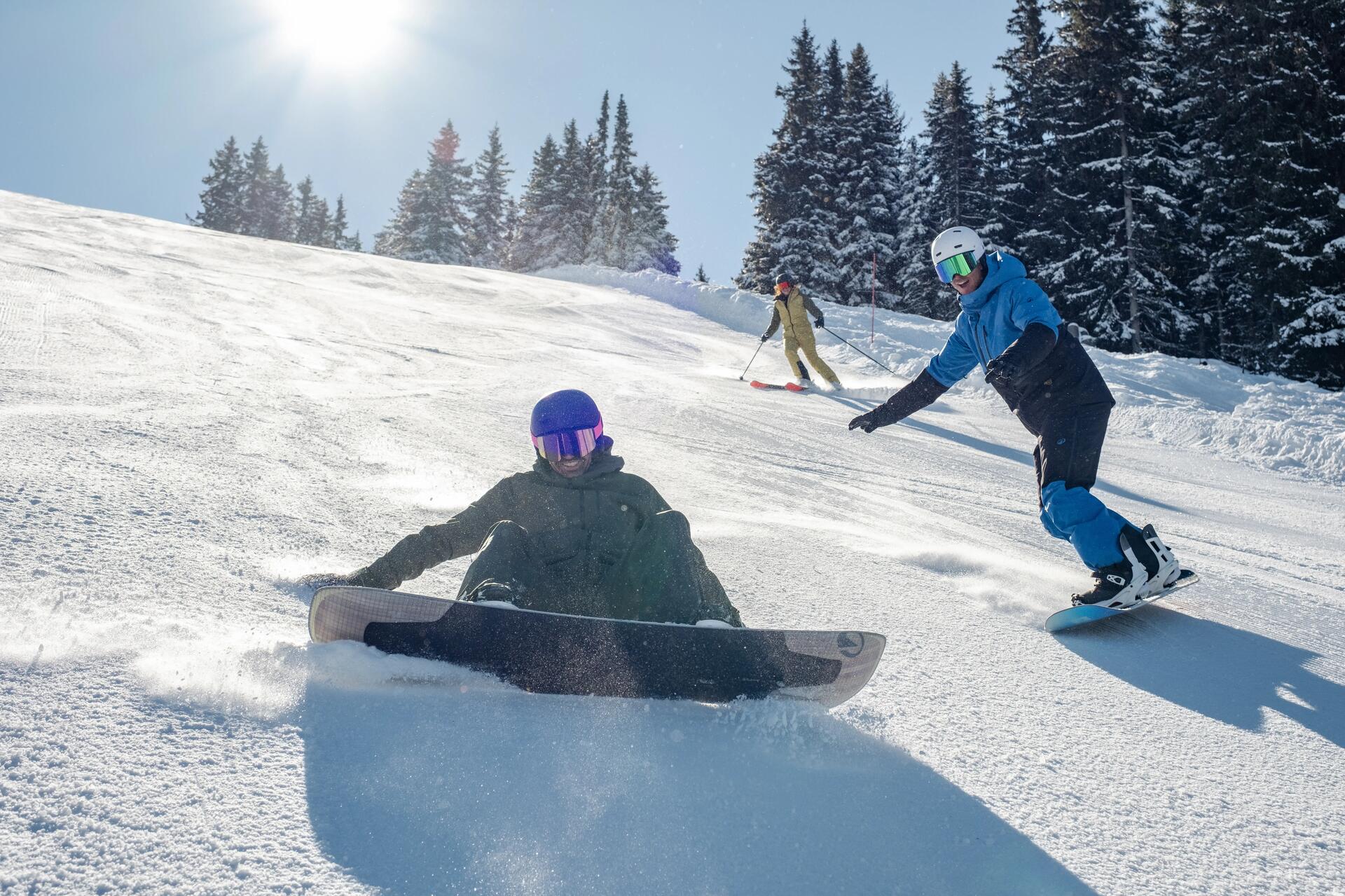 Mężczyna w kasku i goglach snowboardowych siedzący na stoku po upadku na desce snowboardowej