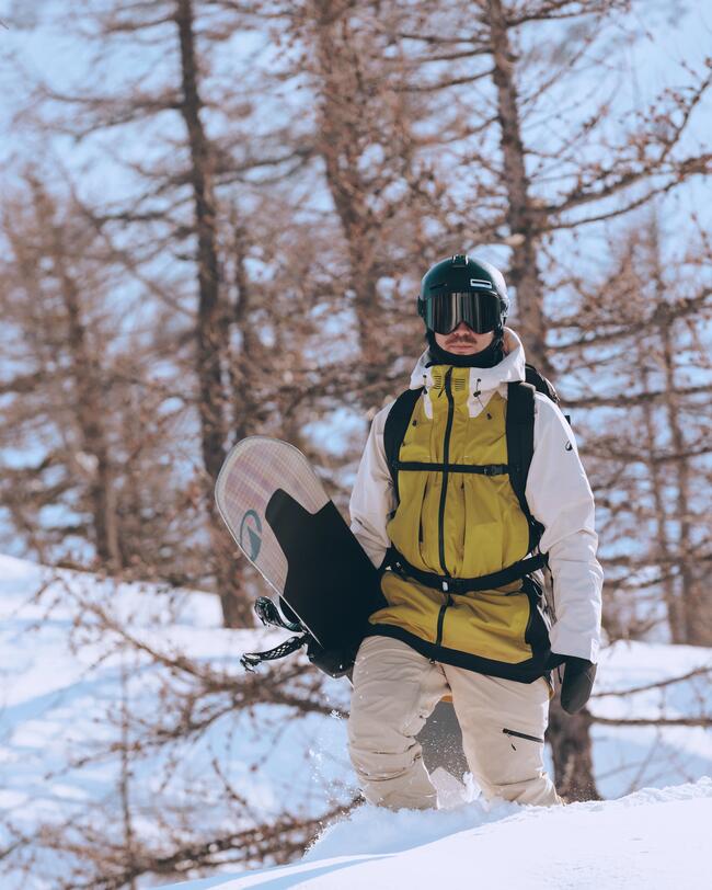 Snowboarder mit gelber Jacke und Schutzausrüstung im Schnee