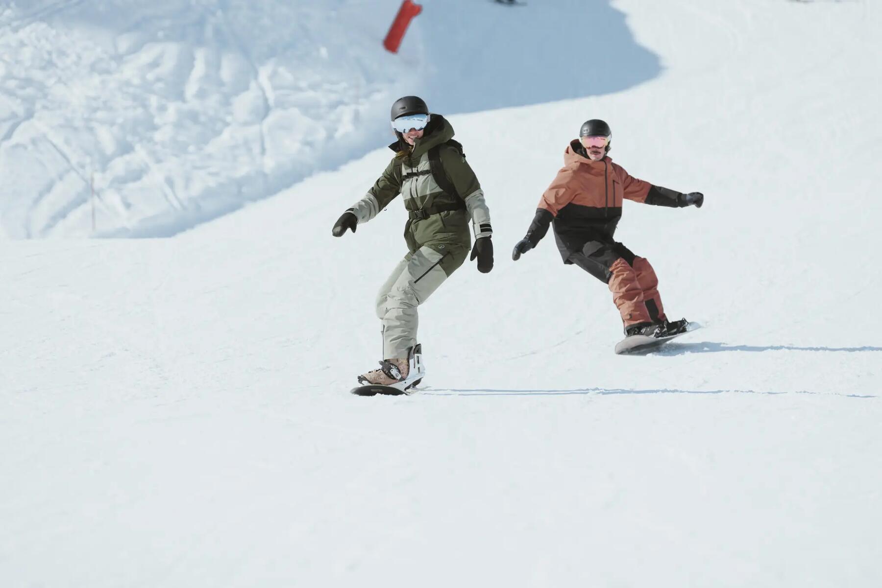 Dwie osoby w kaskach i w goglach jeżdżące na snowboardzie