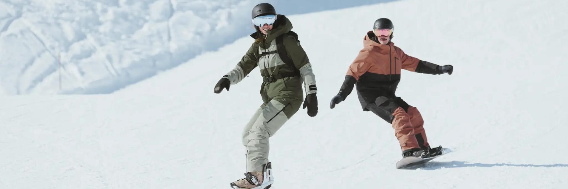 Dwie osoby w kaskach i w goglach jeżdżące na snowboardzie