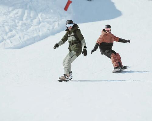 Dwie osoby w kasku i w goglach jeżdżące na snowboardzie