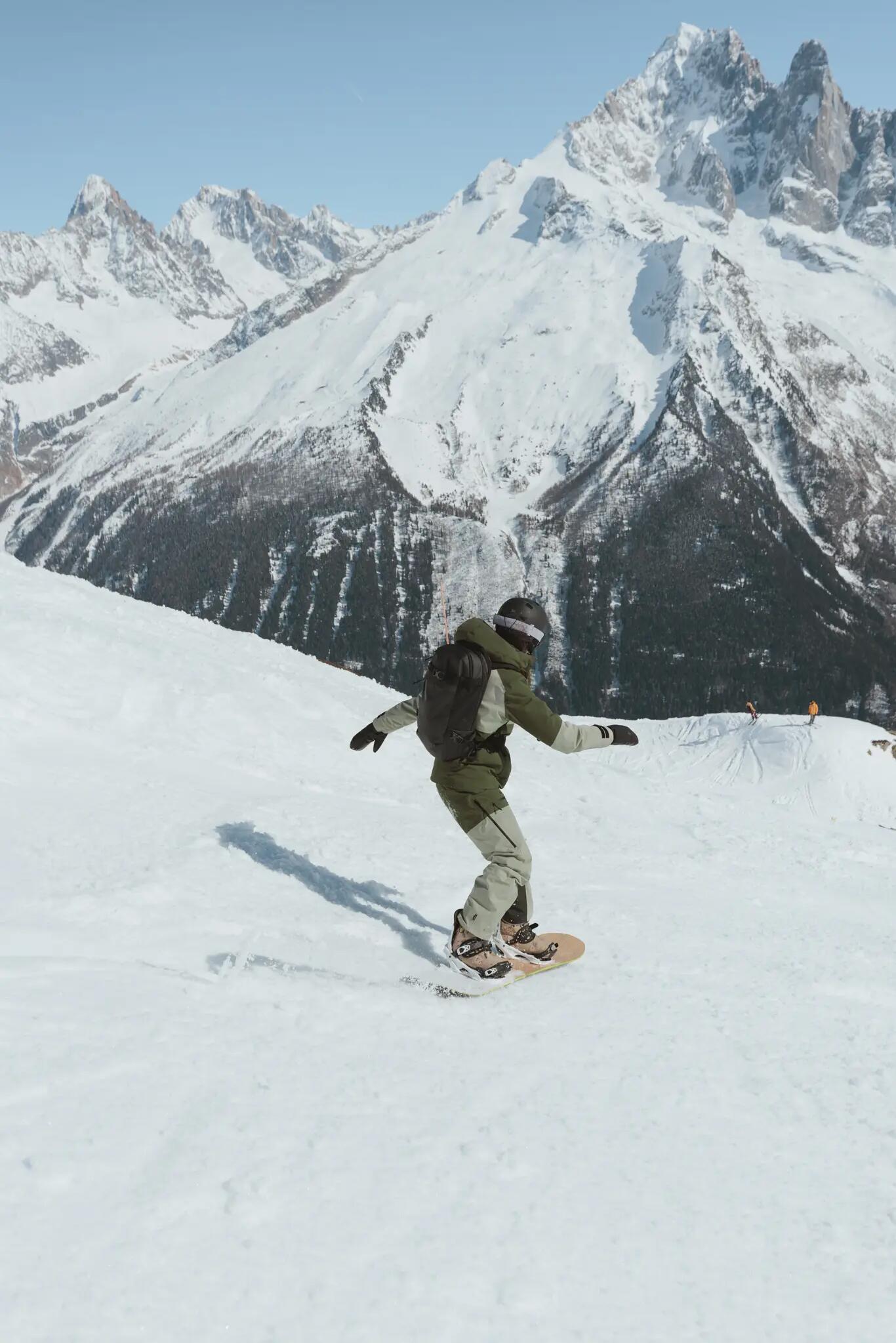 Mężczyzna w kasku i w goglach z plecakiem jeżdżący na snowboardzie
