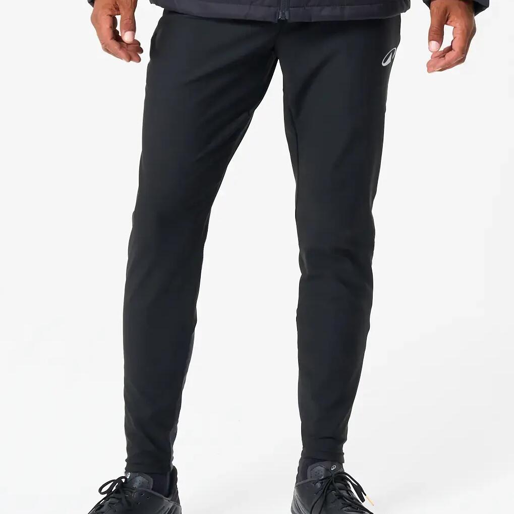 Angezogene schwarze Fußballhose mit Fußballschuhen vor weißer Wand.