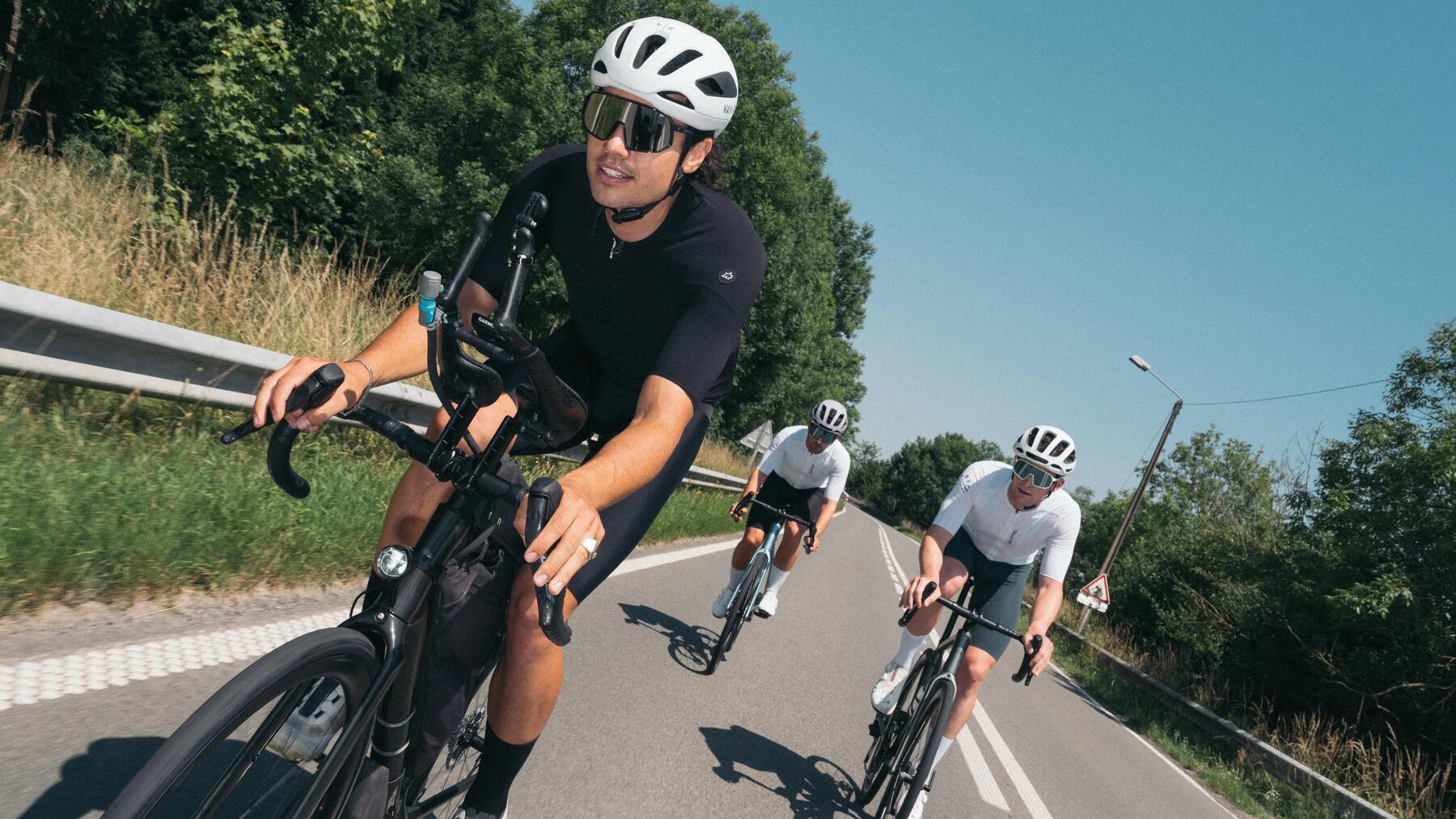 Mężczyźni w kaskach rowerowych jadący na rowerach szosowych drogą