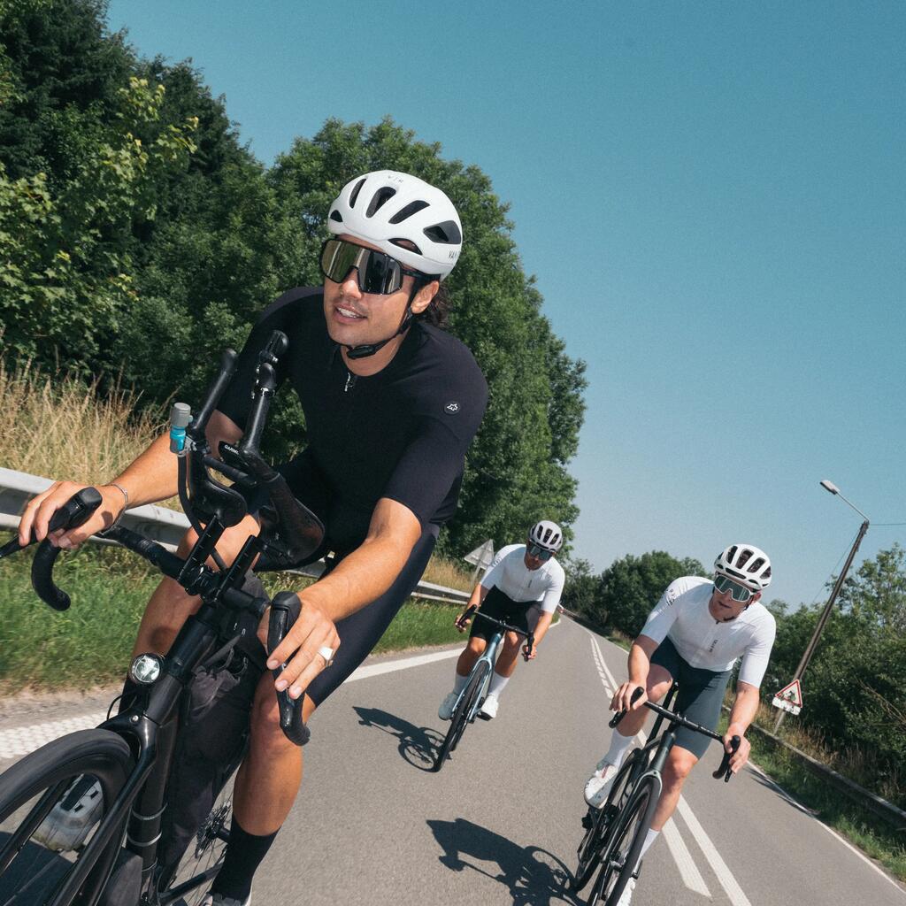 Trojica moških kolesari po cesti n a cestnih kolesih v belem dresu in beli čeladi.