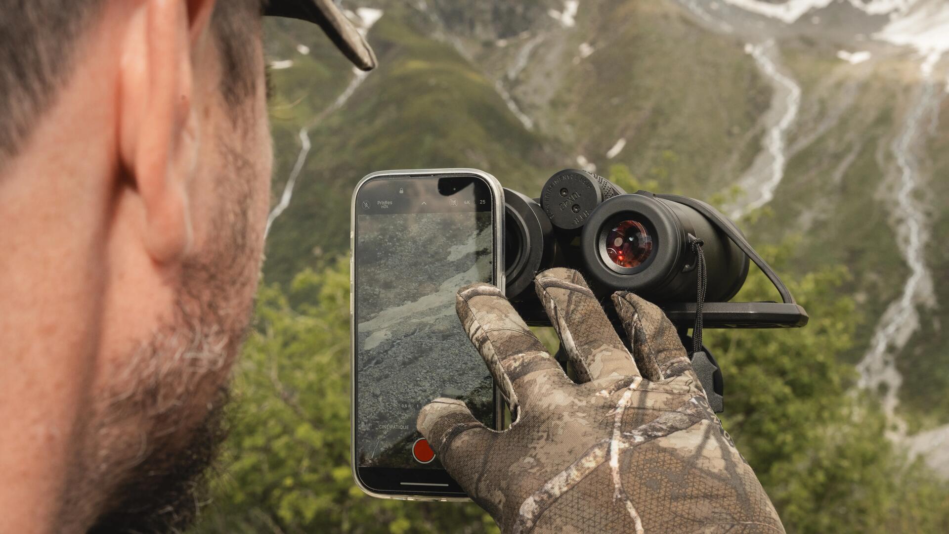 Un chasseur à l'approche fait de la digiscopie avec son smartphone et sa paire de jumelles