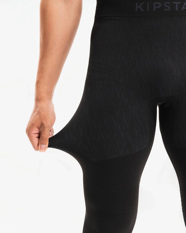 Person trägt schwarze Keepdry-Tight und zieht daran. Aufnahme von vorne vor weißem Hintergrund.