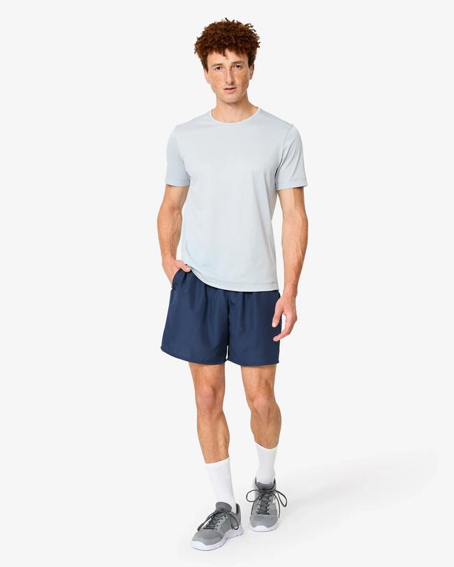 Junger Mann in hellem T-Shirt, dunkelblauer Sporthose und Sportschuhen posiert frontal.