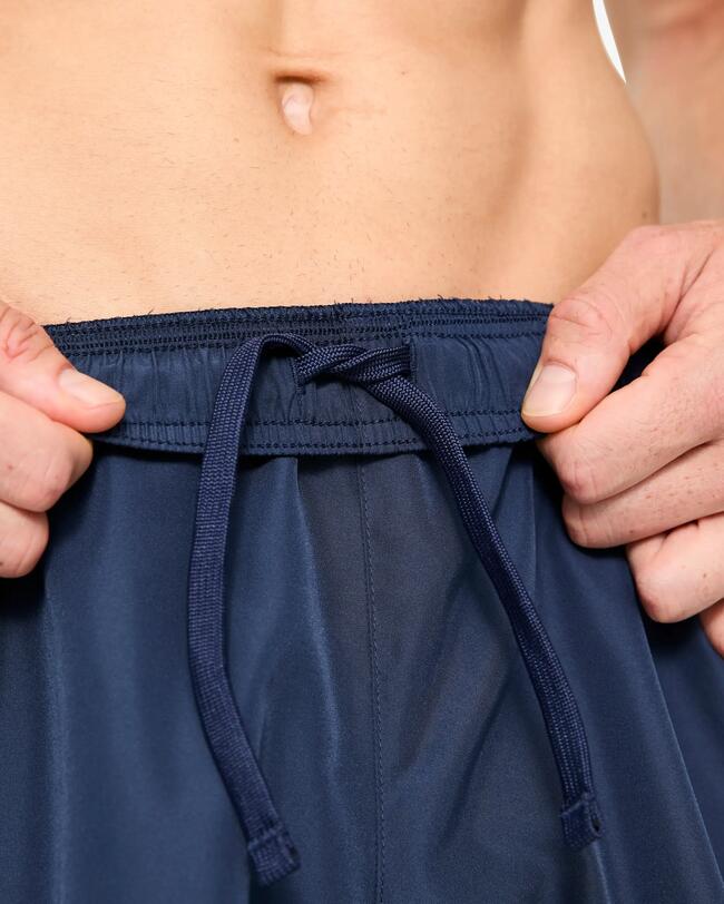Nahaufnahme: Hände ziehen an der Kordel des Bundes einer dunkelblauen Sporthose.