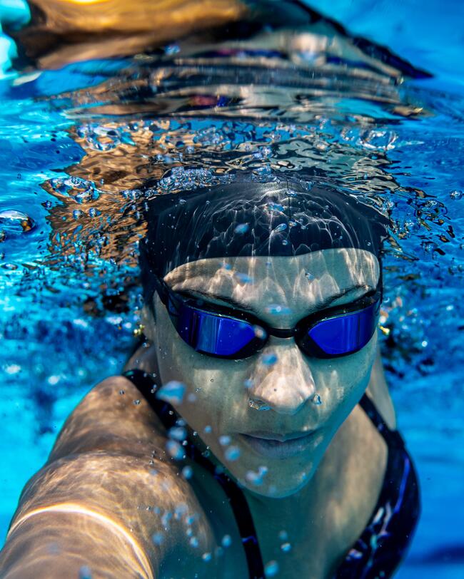 Frau schwimmt in Schwimmbecken, frontalansicht, Schwimmbrille, Badekappe, Badeanzug, konzentrierter Blick