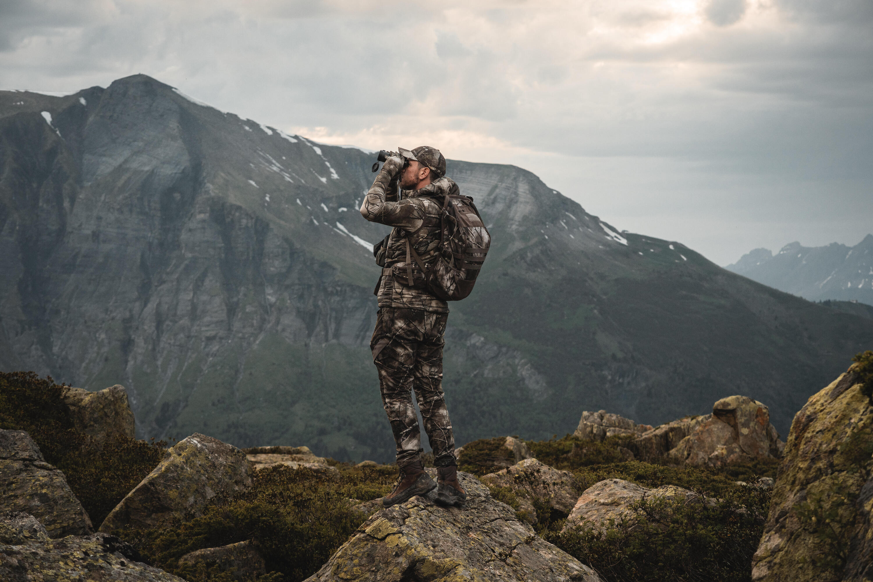 Un chasseur à l'approche en montagne qui observe le paysage avec ses jumelles au milieu de rochers