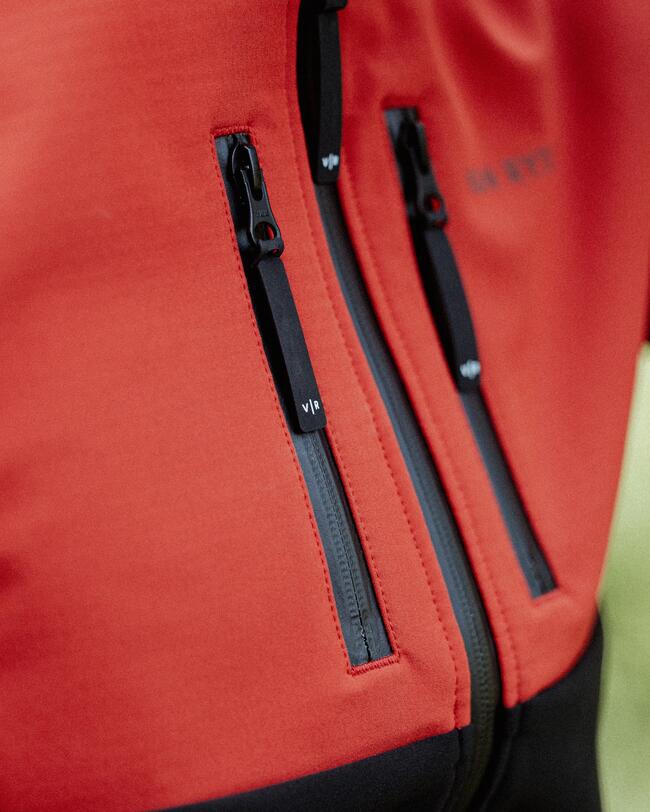 Rote Jacke mit zwei senkrechten, schwarzen Reißverschlüssen, glatte Oberfläche, dezente schwarze Akzente.