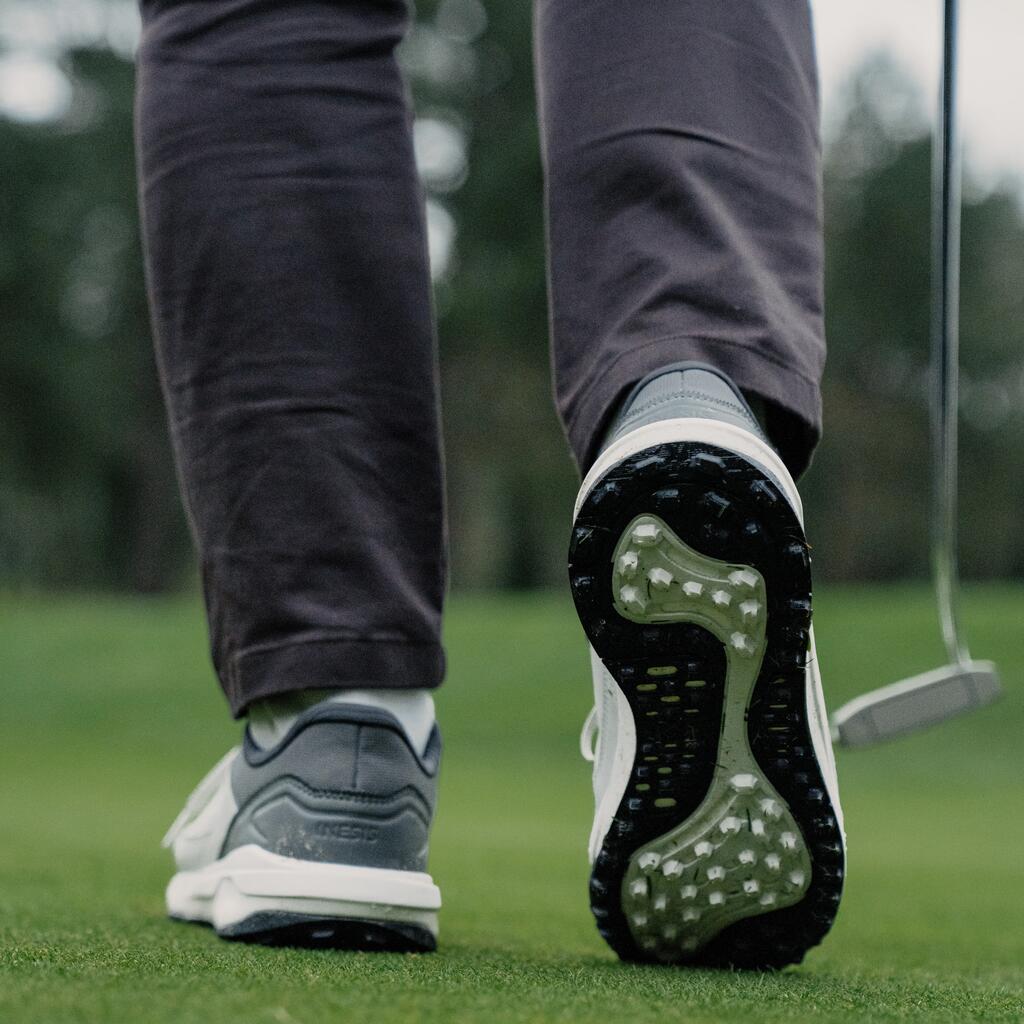 Nahaufnahme von hinten auf die Beine und Golfschuhe eines Spielers, der über das Grün geht, mit Putter an der Seite.